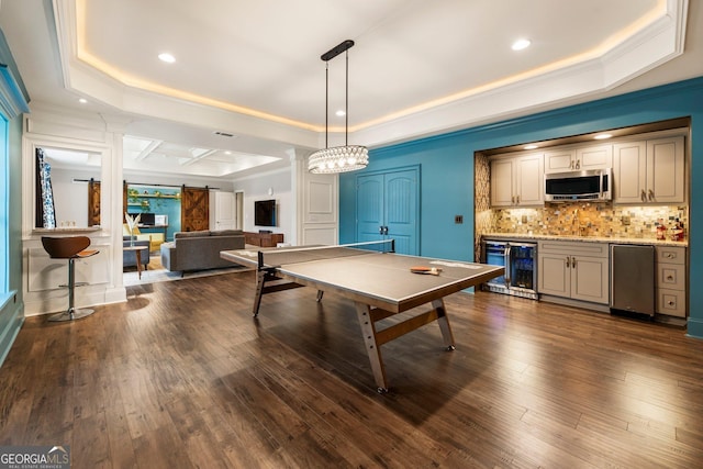 game room featuring crown molding, beverage cooler, a barn door, a tray ceiling, and dark wood-style flooring