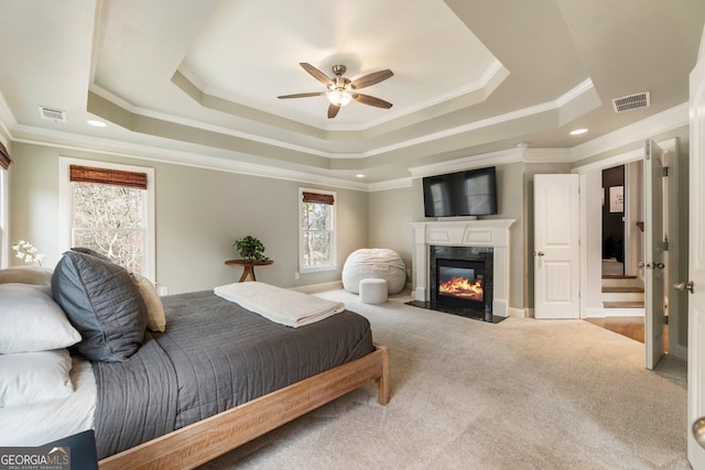 bedroom with a raised ceiling, visible vents, carpet floors, and a premium fireplace