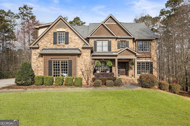 craftsman house featuring brick siding, a front yard, and roof with shingles