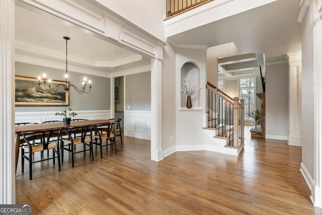 dining room featuring a notable chandelier, ornamental molding, wood finished floors, stairway, and a decorative wall