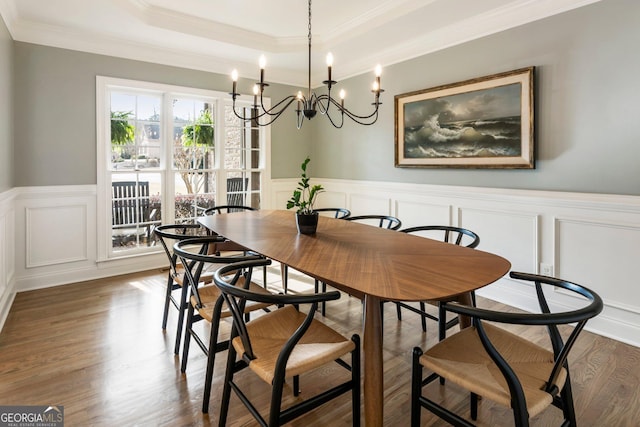 dining area with a wainscoted wall, a tray ceiling, wood finished floors, crown molding, and a decorative wall