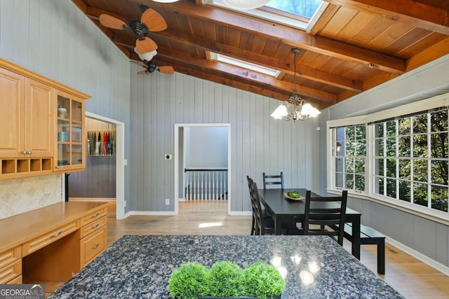 dining space with light wood finished floors, vaulted ceiling with skylight, wooden ceiling, baseboards, and ceiling fan with notable chandelier