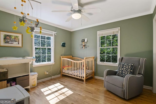 bedroom featuring ornamental molding, a crib, multiple windows, and wood finished floors