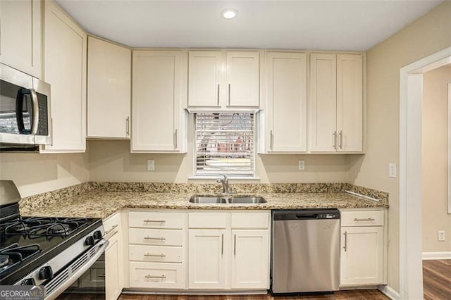 kitchen featuring appliances with stainless steel finishes, a sink, cream cabinetry, and light stone countertops