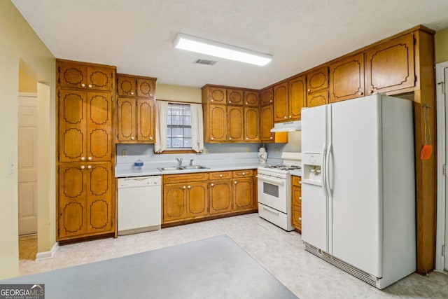 kitchen featuring white appliances, visible vents, brown cabinetry, under cabinet range hood, and a sink