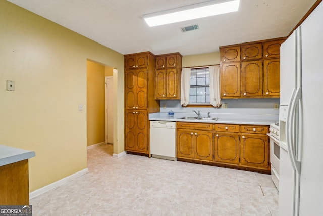 kitchen featuring white appliances, a sink, visible vents, light countertops, and brown cabinets