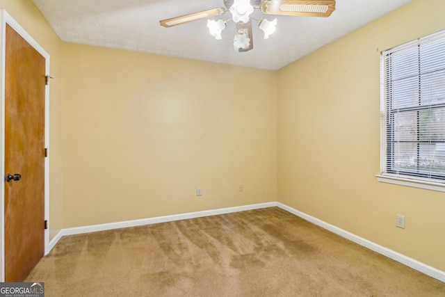 carpeted spare room featuring ceiling fan and baseboards