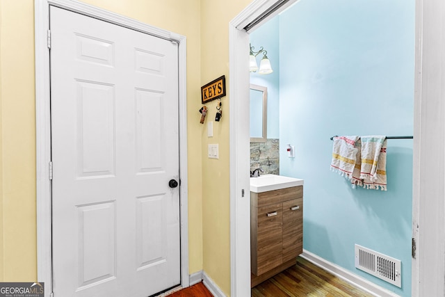 bathroom with tasteful backsplash, visible vents, vanity, wood finished floors, and baseboards