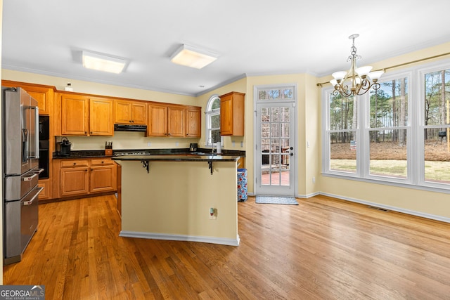 kitchen with high end fridge, light wood finished floors, dark countertops, and a kitchen breakfast bar