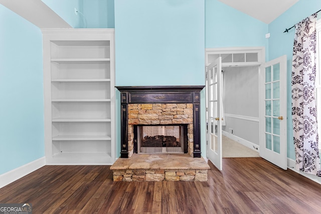 unfurnished living room with vaulted ceiling, a stone fireplace, french doors, and wood finished floors