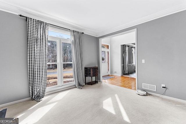 carpeted spare room with baseboards, visible vents, a wealth of natural light, and ornamental molding