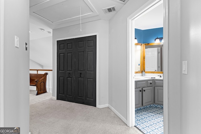 corridor with light carpet, a sink, visible vents, baseboards, and attic access