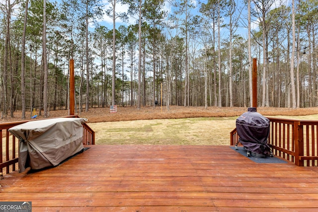 wooden terrace featuring a lawn, grilling area, and a forest view