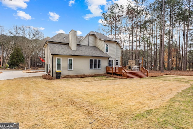 back of house with roof with shingles, a chimney, a deck, and a yard