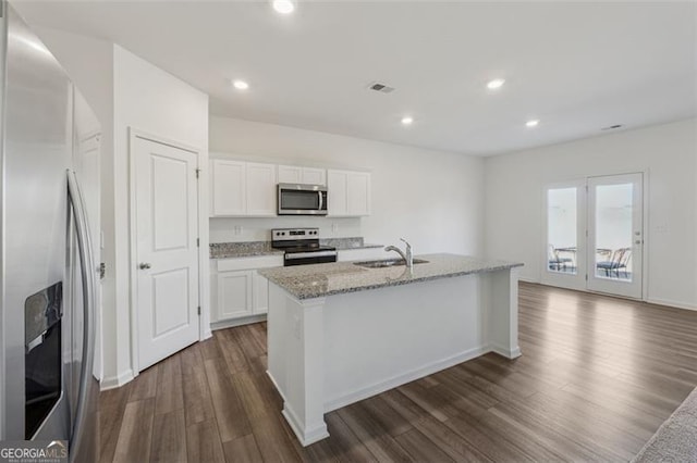 kitchen featuring light stone counters, a center island with sink, stainless steel appliances, dark wood-type flooring, and a sink