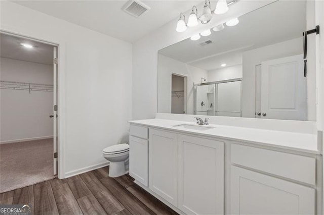 full bathroom featuring a stall shower, visible vents, toilet, wood finished floors, and vanity