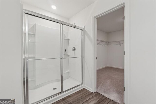 bathroom with a stall shower, baseboards, a walk in closet, and wood finished floors