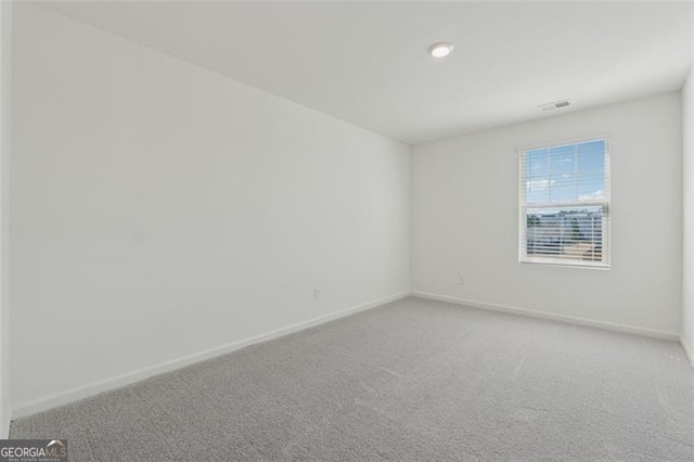 spare room featuring light colored carpet, visible vents, and baseboards