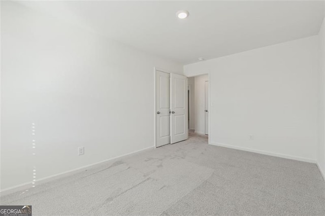 spare room featuring light colored carpet and baseboards