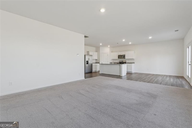 unfurnished living room featuring dark wood-type flooring, recessed lighting, dark carpet, and baseboards