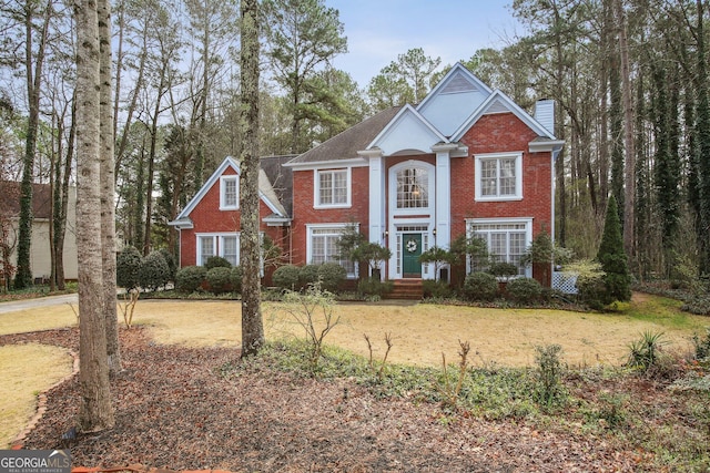 neoclassical home featuring a front yard, a chimney, and brick siding