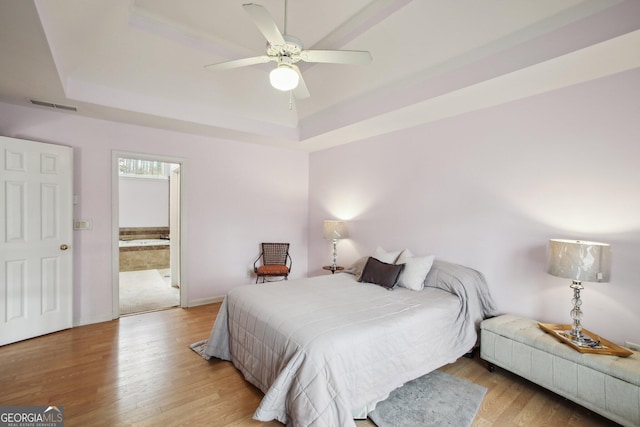 bedroom featuring a raised ceiling, visible vents, light wood-style flooring, a ceiling fan, and baseboards