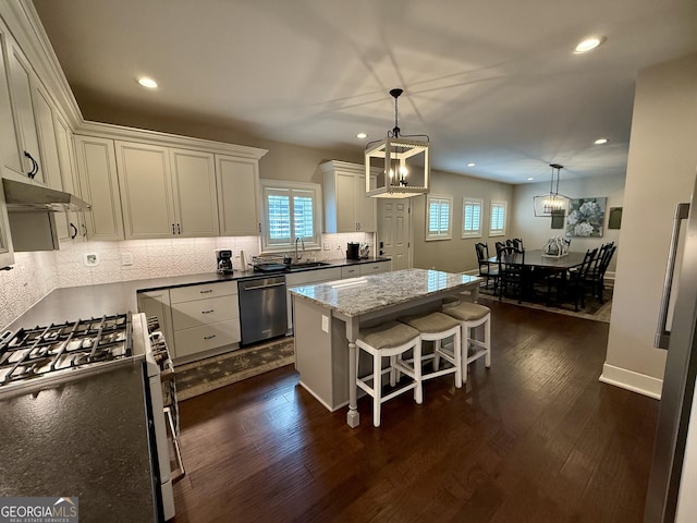 kitchen featuring a chandelier, dark wood-type flooring, a sink, appliances with stainless steel finishes, and a center island