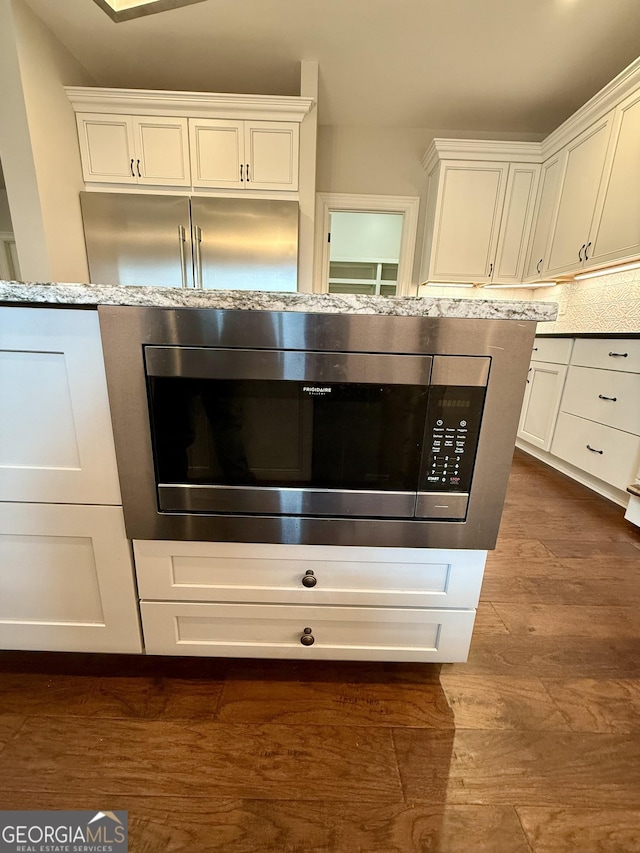 room details featuring white cabinetry, stainless steel microwave, dark wood finished floors, and backsplash