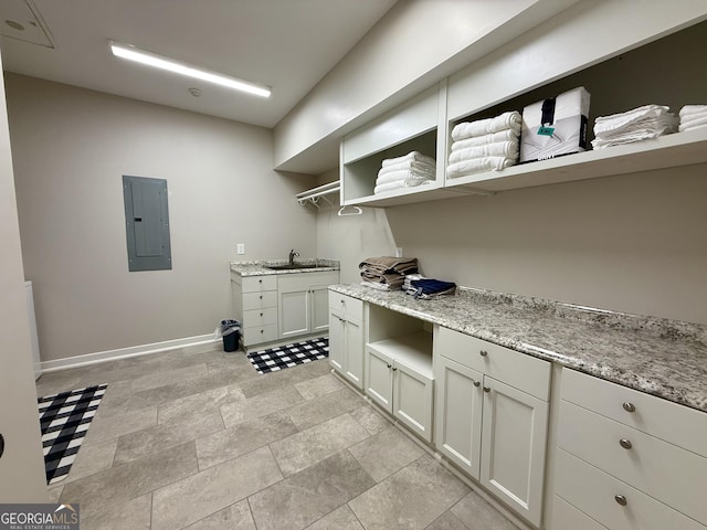 kitchen with light stone counters, open shelves, a sink, electric panel, and baseboards