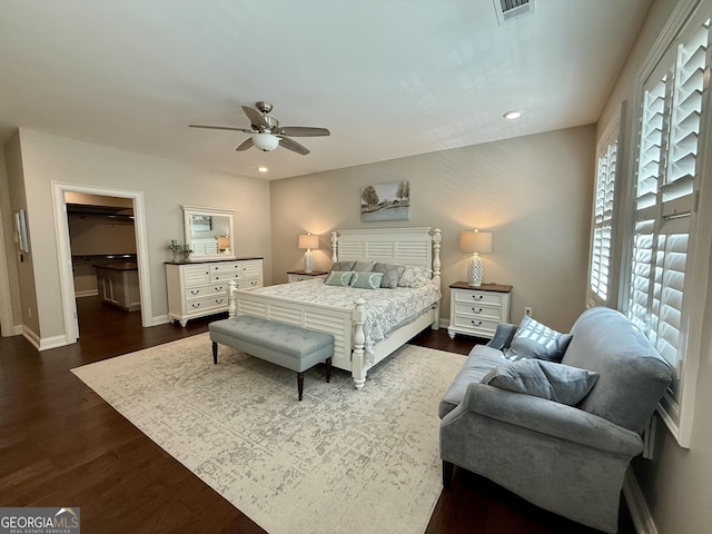 bedroom with a walk in closet, dark wood finished floors, recessed lighting, visible vents, and baseboards