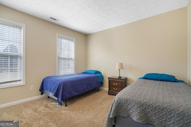 bedroom with a textured ceiling, carpet floors, visible vents, and baseboards