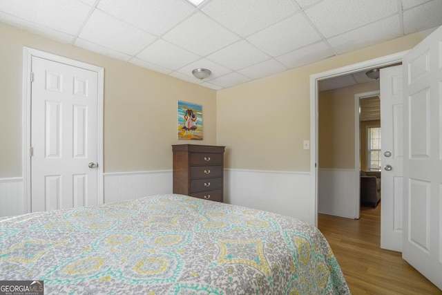 bedroom featuring wainscoting, wood finished floors, and a paneled ceiling