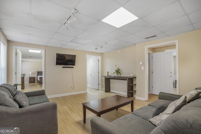 living room featuring rail lighting, visible vents, light wood-type flooring, a drop ceiling, and baseboards