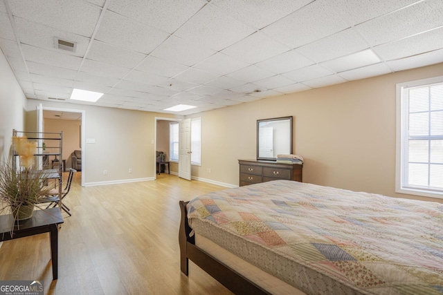 bedroom with light wood-type flooring, a drop ceiling, visible vents, and baseboards