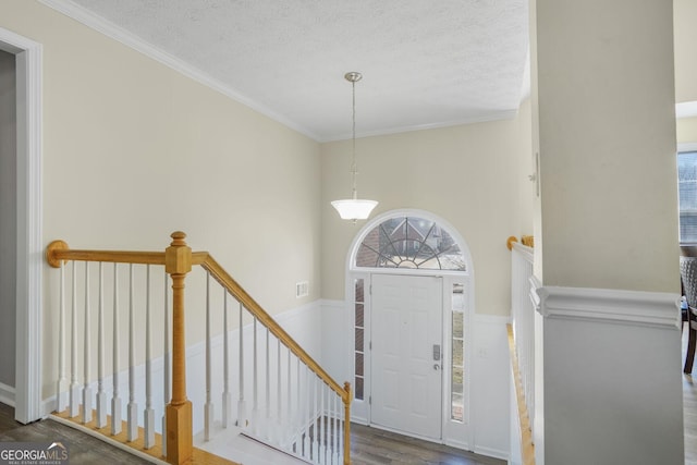 entrance foyer featuring ornamental molding, visible vents, a textured ceiling, and wood finished floors