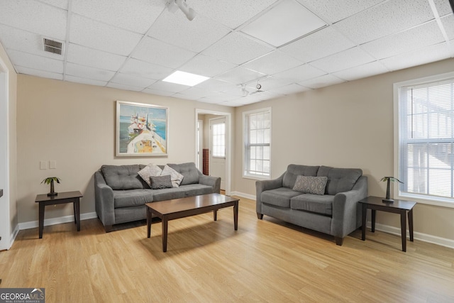 living room featuring a paneled ceiling, light wood-type flooring, visible vents, and baseboards