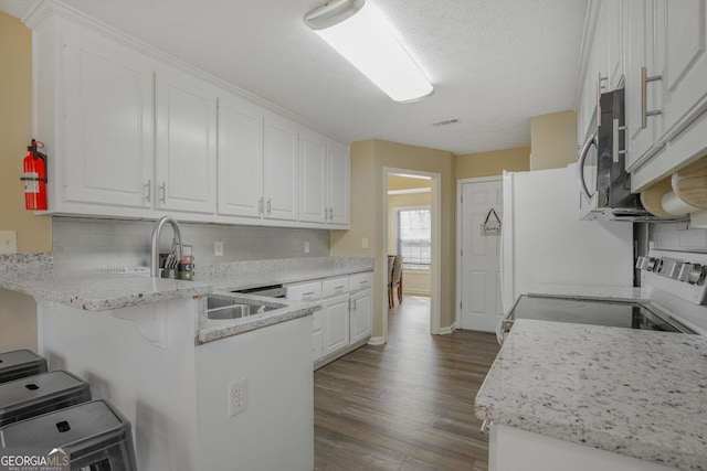 kitchen featuring electric range, dark wood finished floors, stainless steel microwave, a peninsula, and white cabinetry