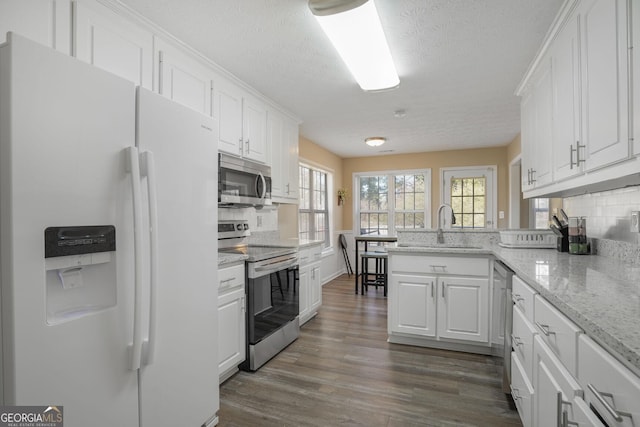 kitchen with dark wood-style flooring, stainless steel appliances, white cabinets, a sink, and a peninsula