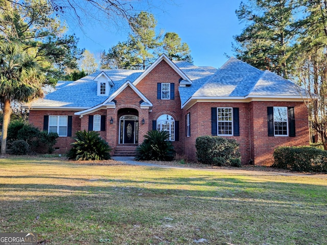 traditional home featuring brick siding, crawl space, a front yard, and a shingled roof