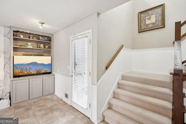 stairs featuring tile patterned flooring, a wainscoted wall, and visible vents