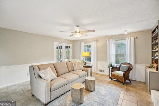 living room with ceiling fan, french doors, wainscoting, and visible vents