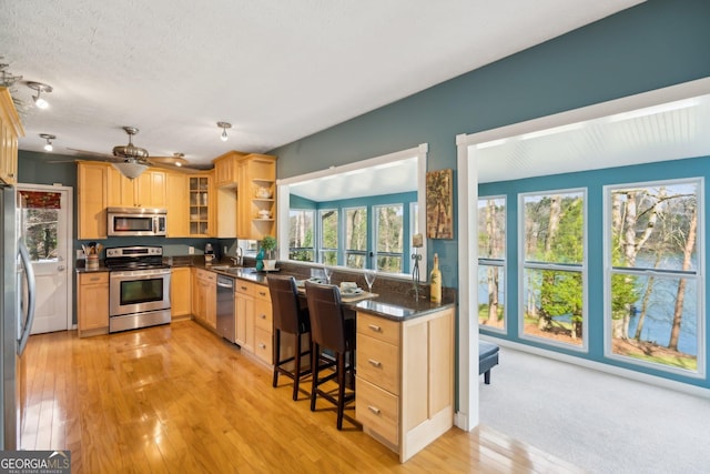 kitchen featuring open shelves, stainless steel appliances, dark countertops, light wood-style floors, and a sink