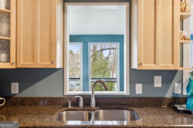 kitchen with glass insert cabinets, a sink, and dark stone countertops