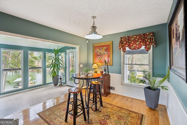 dining room featuring hardwood / wood-style flooring, visible vents, a textured ceiling, and a wainscoted wall