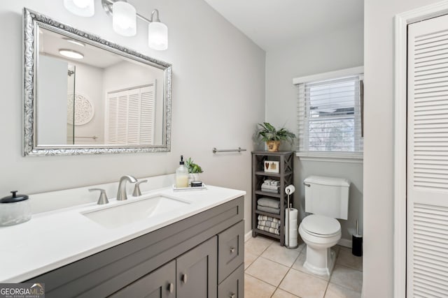 bathroom with baseboards, toilet, tile patterned flooring, vanity, and a closet