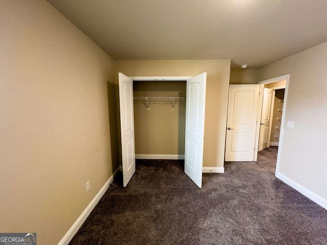 unfurnished bedroom featuring baseboards, dark colored carpet, and a closet