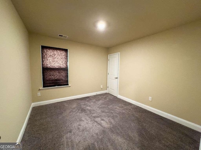 empty room with dark colored carpet, visible vents, and baseboards