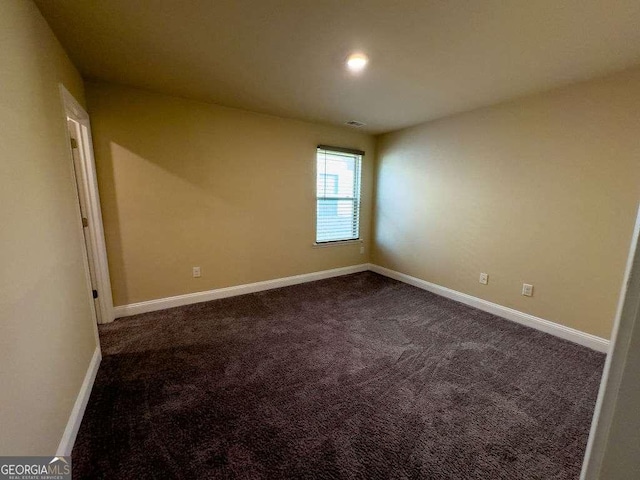 unfurnished room featuring baseboards and dark colored carpet