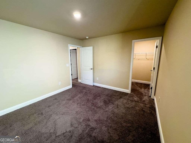 unfurnished bedroom featuring carpet, a spacious closet, and baseboards