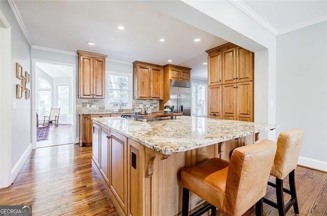 kitchen featuring light wood-type flooring, stainless steel built in fridge, a kitchen island, tasteful backsplash, and light stone countertops